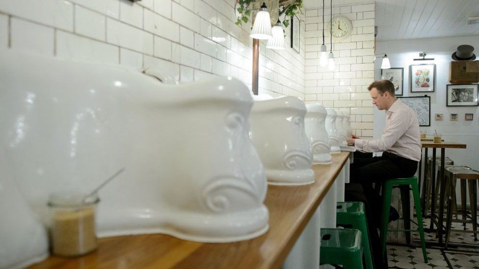 A man sits on the counter with original urinals in "Attendant", a former public toilet that has been converted into a coffee shop and sandwich bar in central London
