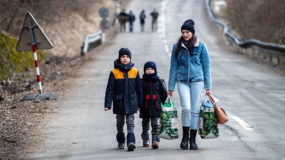 A woman with two children and carrying bags walk on a street to leave Ukraine after crossing the Slovak-Ukrainian border
