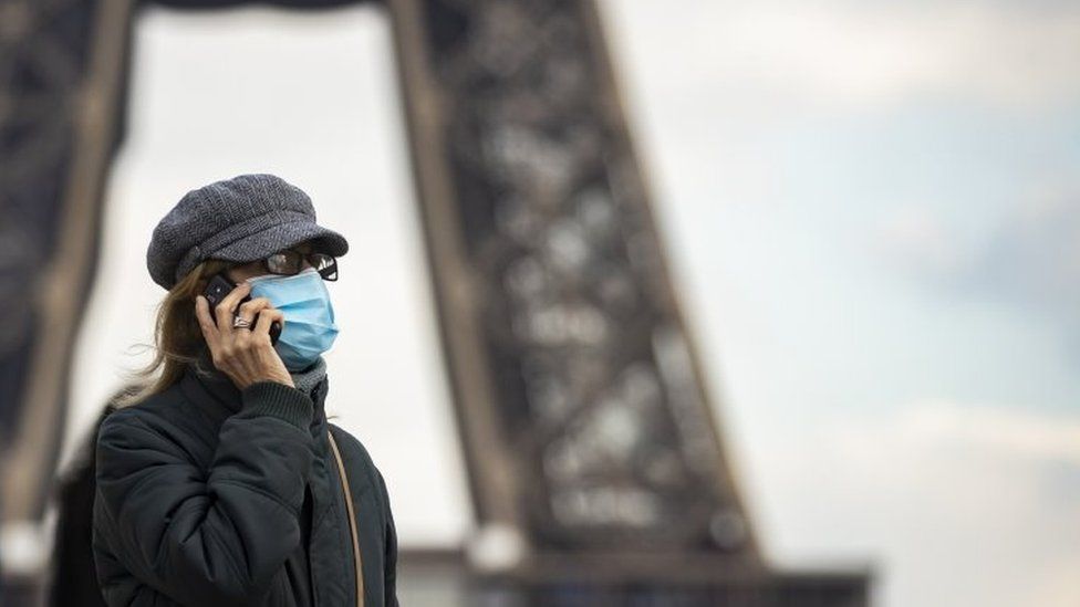 A woman wearing a surgical face mask walks near the Eiffel Tower