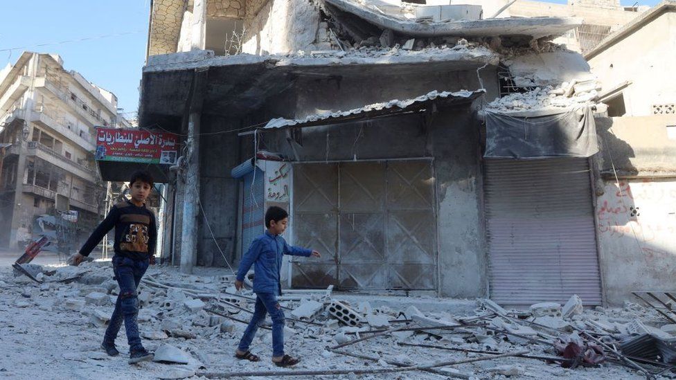 Two children walk past buildings damaged by Syrian army shellfire in Ariha, Idlib (20 October 2021)