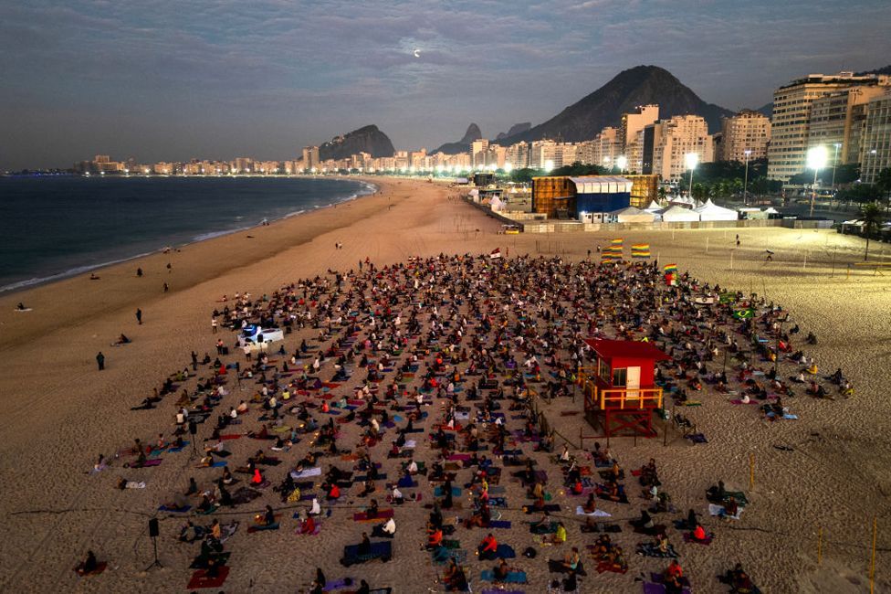 An aerial view shows people taking part in a yoga event at Copacabana beach in Rio de Janeiro, Brazil, on June 22 2024. People sit on the sand of a beach with buildings and mountains in the background