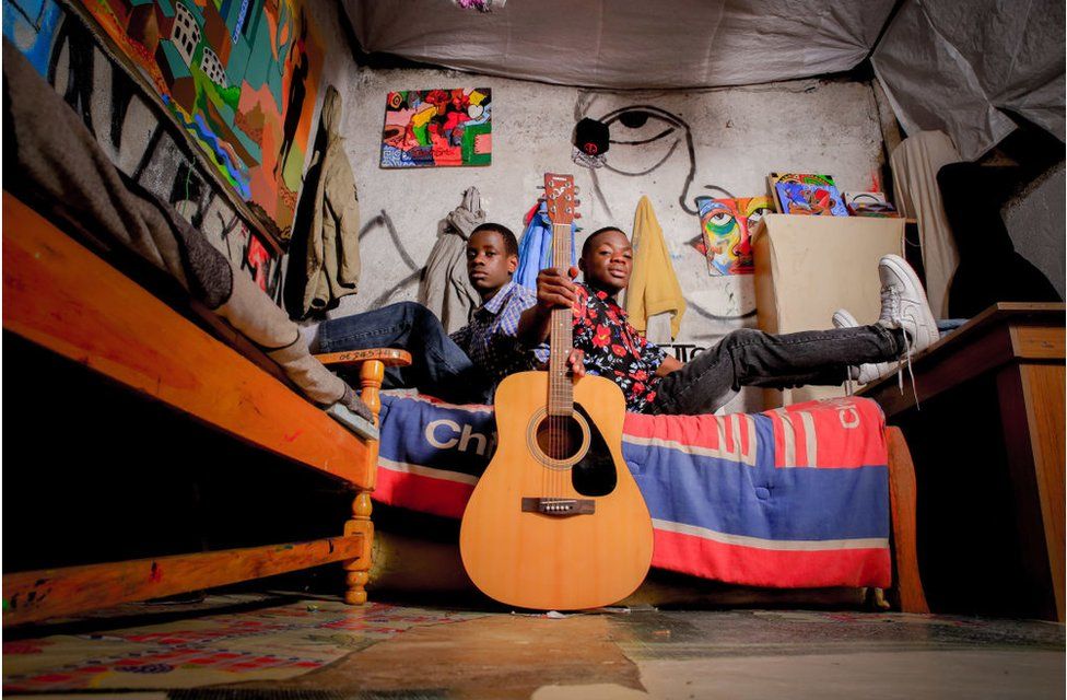 Teenage boys in their bedroom with a guitar.