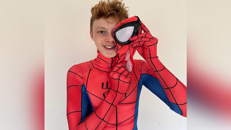 A teenager, Charlie, dressed up as Spiderman. He is wearing the Spiderman suit but not the mask and smiling at the camera