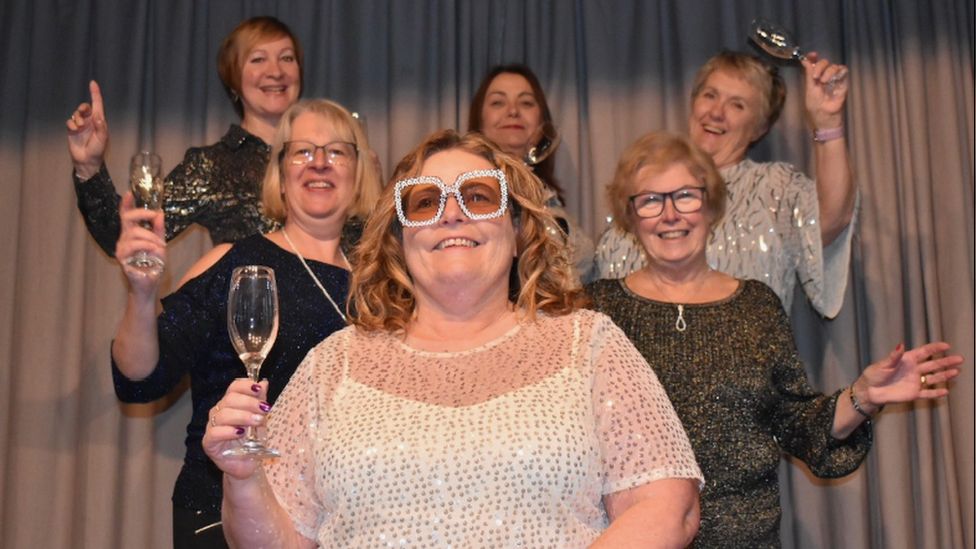 Kate James with members of the Bleadon Women's Institute. They are smiling and laughing and toasting the camera with wine glasses