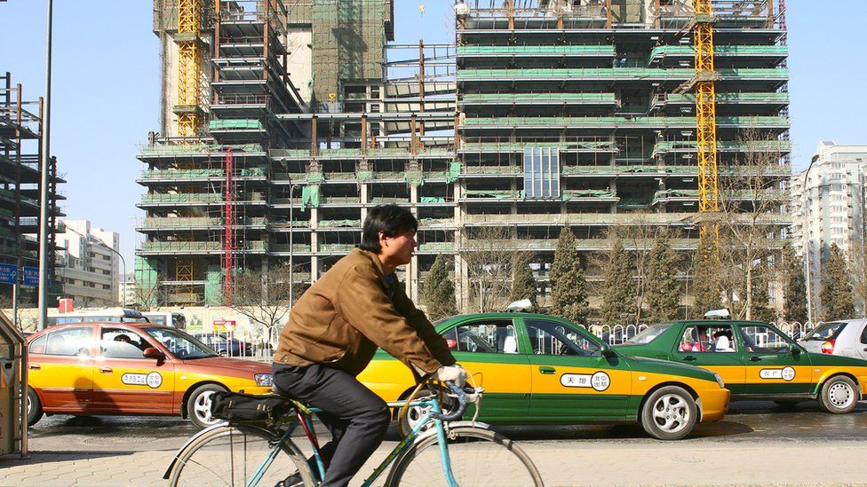 A man rides a bike past a construction site in China