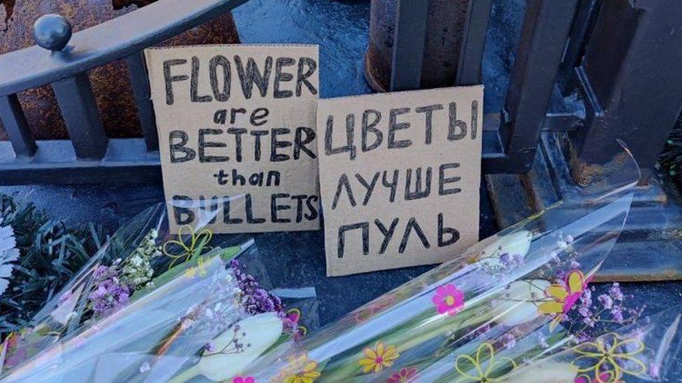 Цветы на мемориале Второй мировой войны в России с табличкой на русском и английском языках, которая гласит: 'цветы лучше пуль'