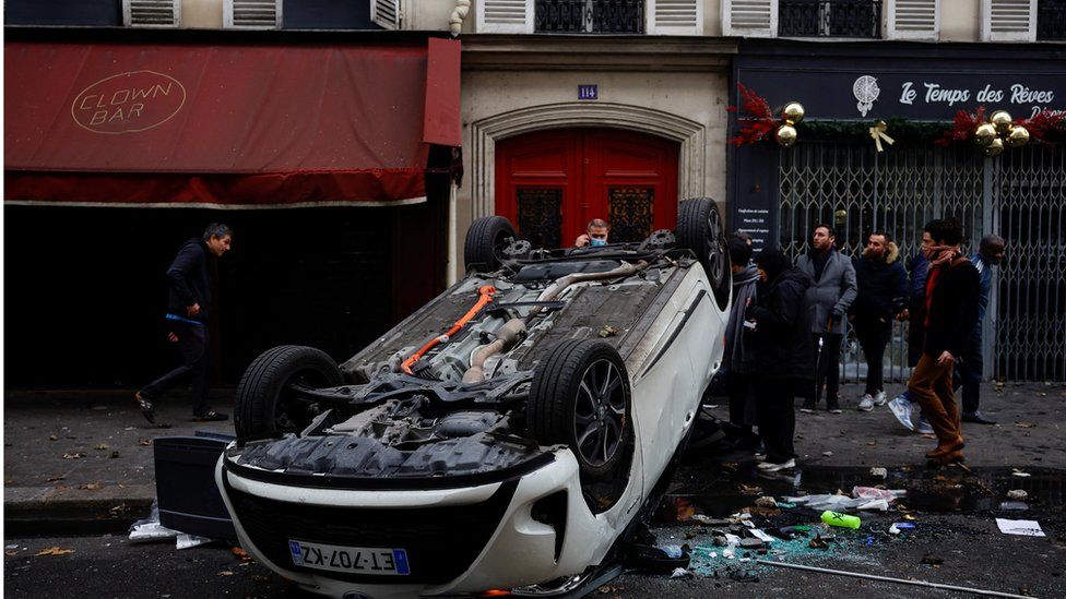 People stand behind an overturned car in central Paris