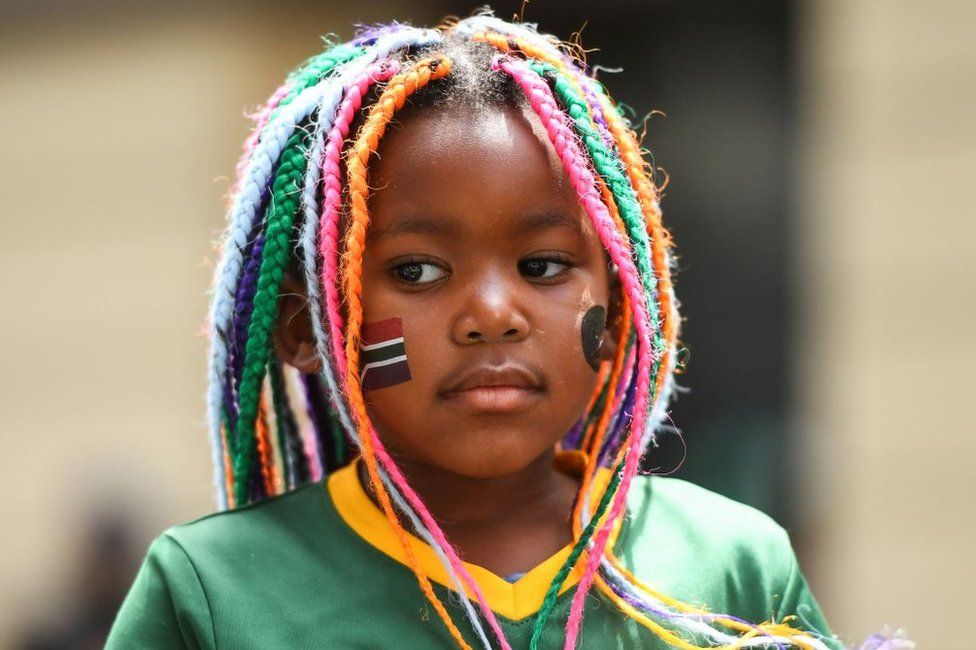 A girl wears a Springboks jersey along with colourful braids and a flag painted on her cheek.