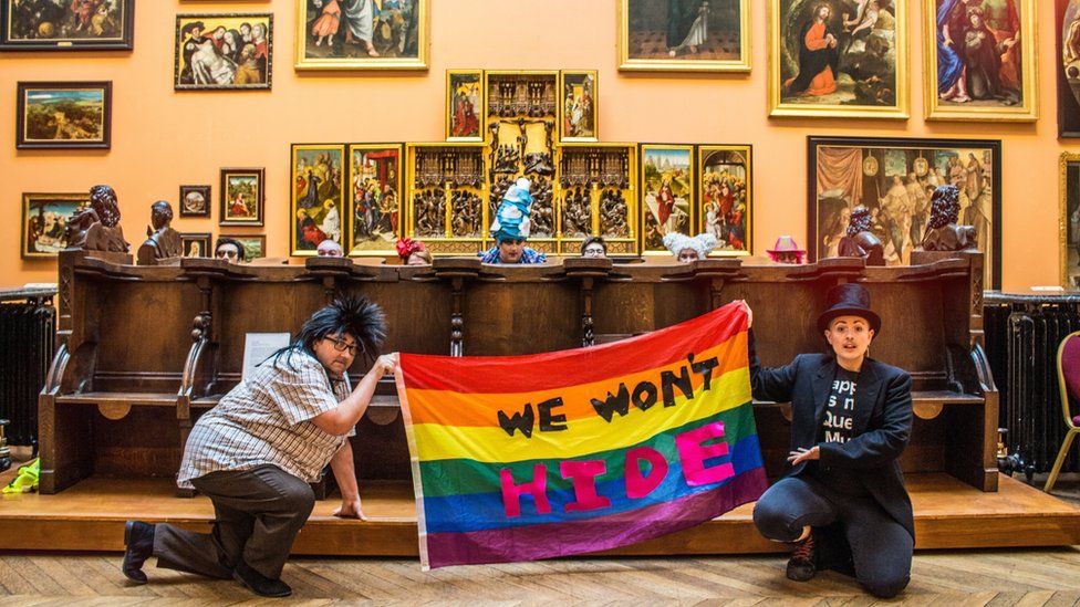Two members of the LGBT+ Northern Social Group hold up a rainbow flag bearing the words: "We won't hide"