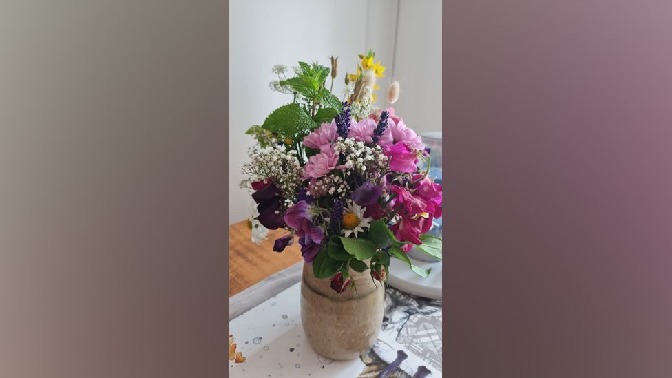 A colourful flower arrangement in a clay vase. The vase is on a table.