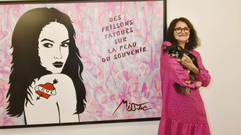 Miss. Tic poses with her dog in front one of her works in Paris, France. Photo: May 2018