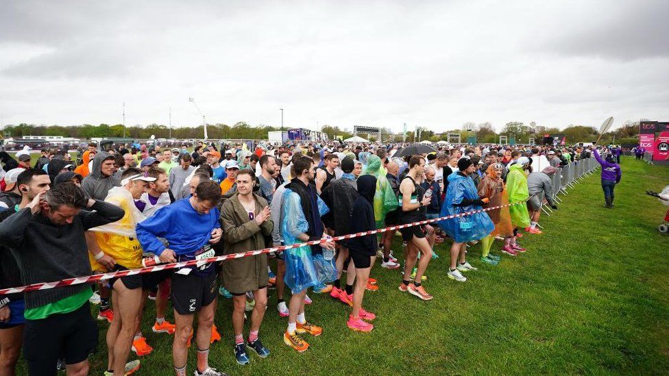 Lines of people in running gear behind a rope in a large field
