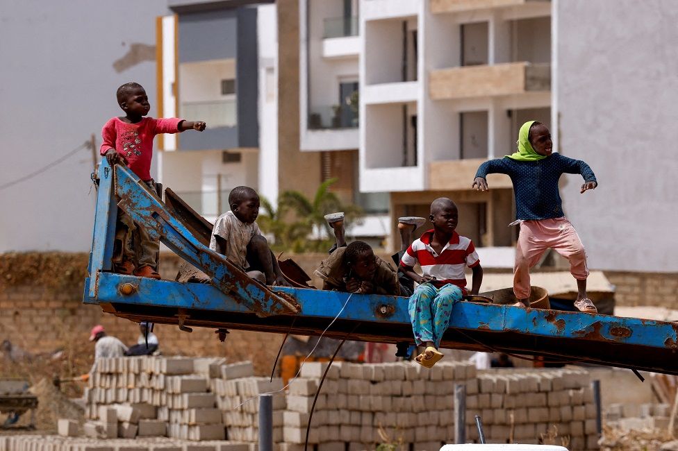 Children play on a truck trailer while watching a car racing on the runway of the old airport in Dakar.