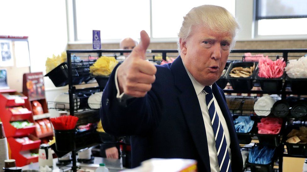 Donald Trump gives a thumbs up to the camera in a petrol station shop