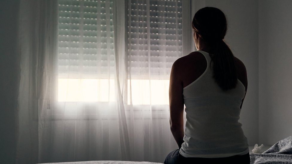 Stock image of woman sitting on a bed, facing a window