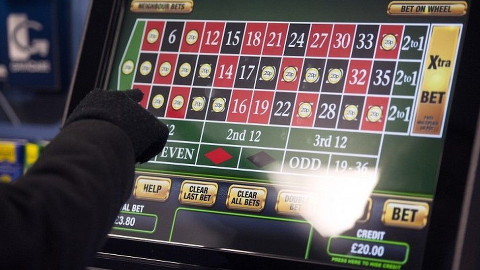 A hand presses the screen of a fixed odds betting terminal