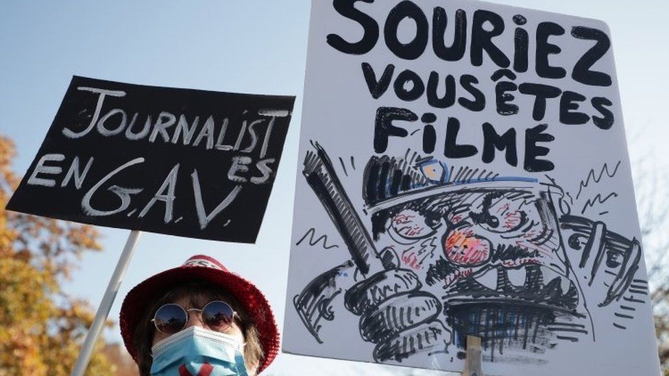 Protesters in Paris hold slogans that read Journalists under arrest (left) and Smile, you're being filmed. Photo: 28 November 2020