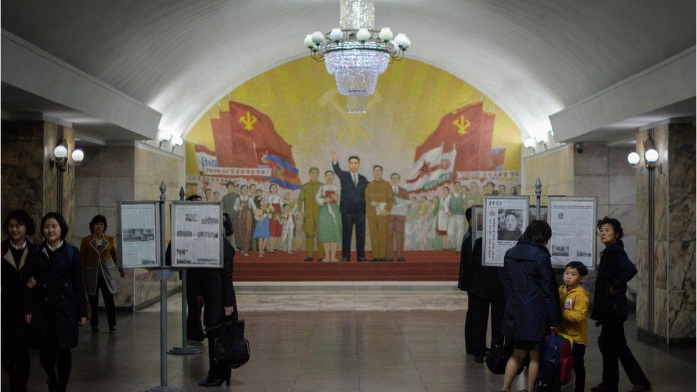 Commuters look at a copy of the Rodong Sinmun newspaper showing an image of North Korea's leader Kim Jong Un, at a newsstand in a subway station in Pyongyang on April 13, 2019