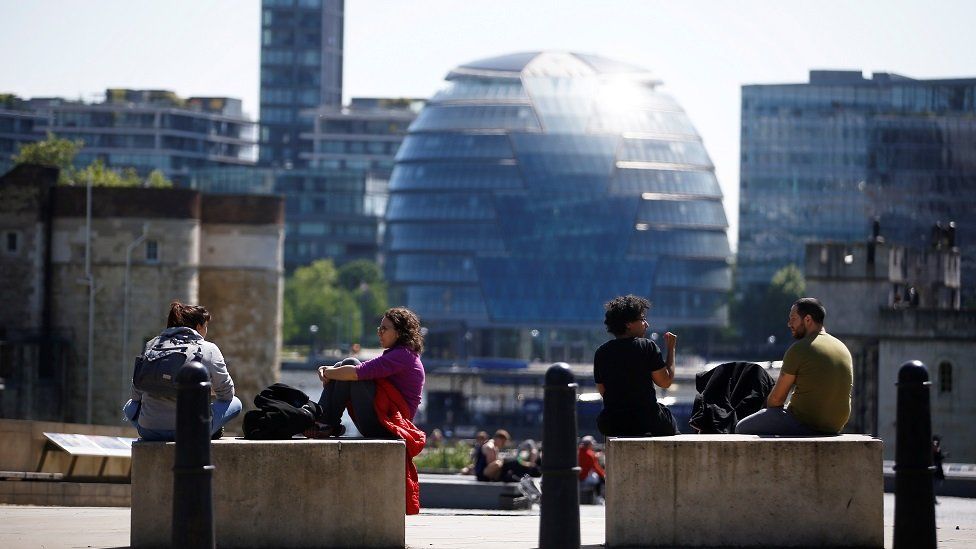 People are seen relaxing in front of City Hall in London, following the outbreak of the coronavirus disease