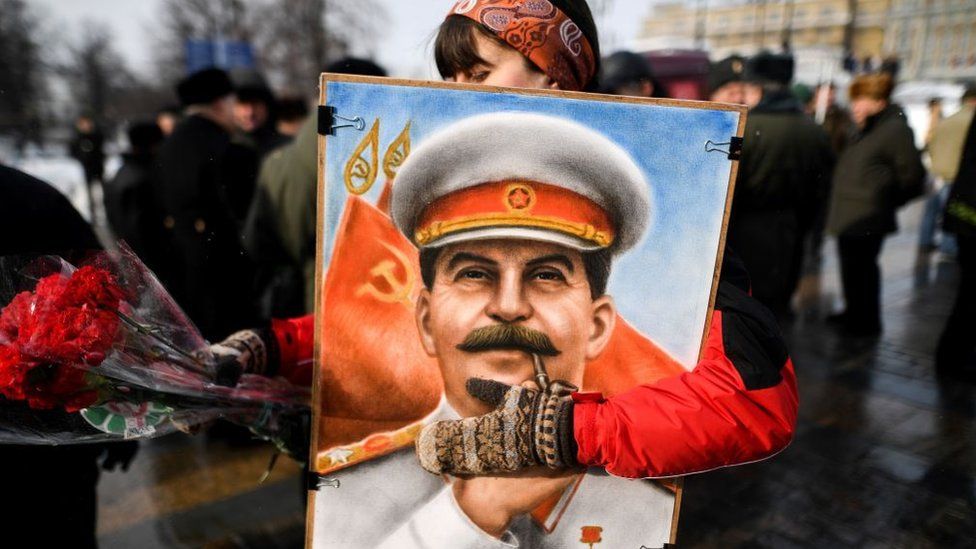 A woman carries a portrait of Joseph Stalin and some fires