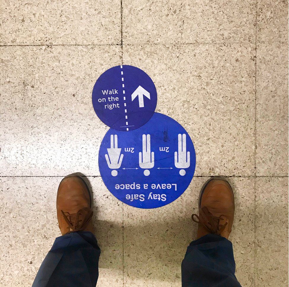 Two blue signs on the ground that ask people to maintain a two-metre distance