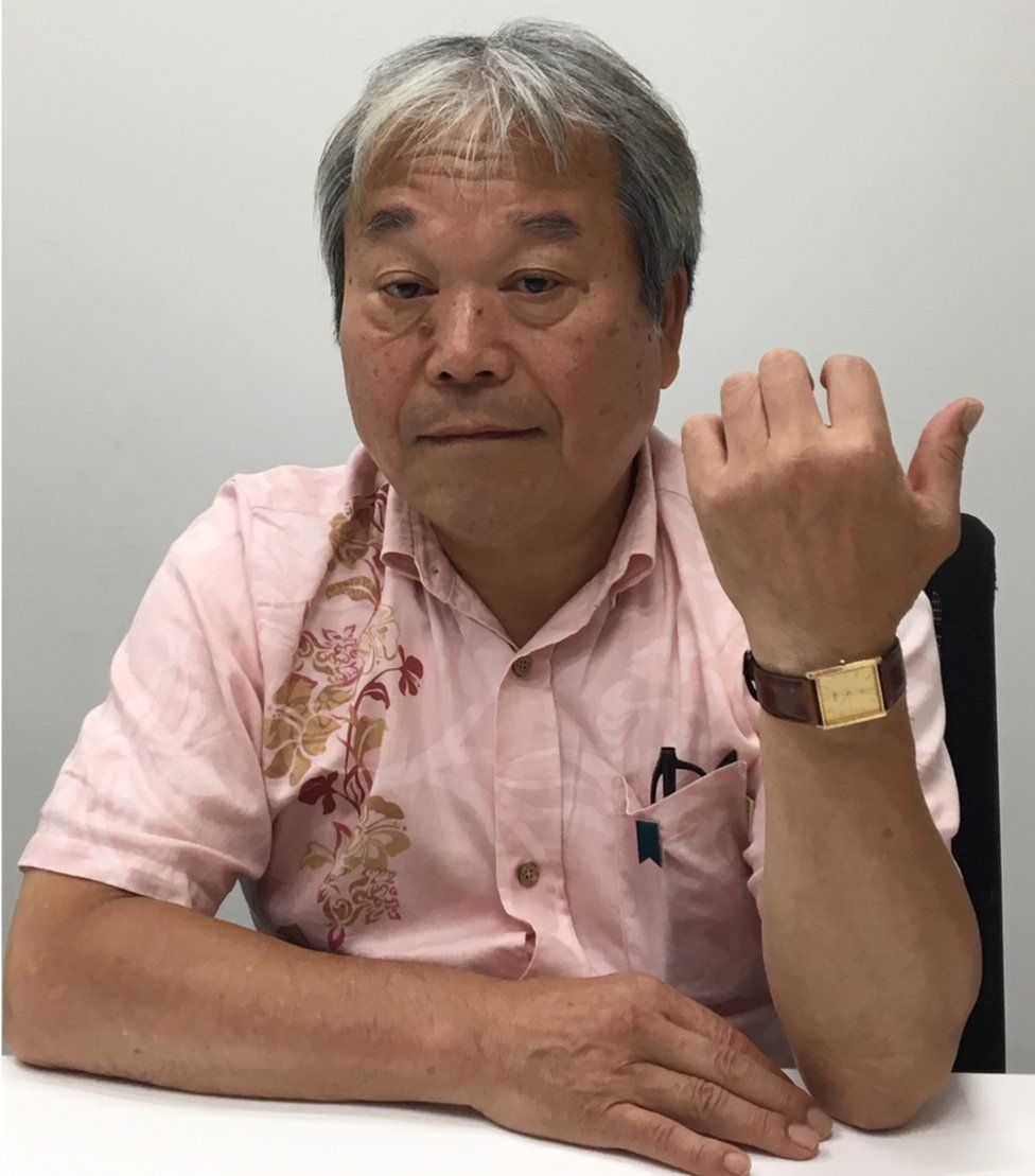 Teruaki Masumoto, in a short-sleeved shirt, holds up his wrist to show a gold watch given to him by his sister before her abduction