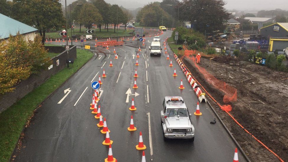 Cars driving through lanes off the roundabout lined with traffic cones.