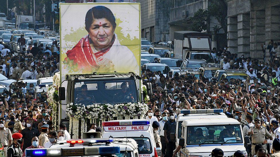 A crowd of people on the road pays tribute to the legendary singer Lata Mangeshkar during the funeral procession in Mumbai.