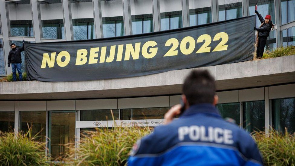 A policeman talks on the phone as Tibetan activists from the Students for a Free Tibet association hang a banner during a protest in front of the International Olympic Committee (IOC) headquarters