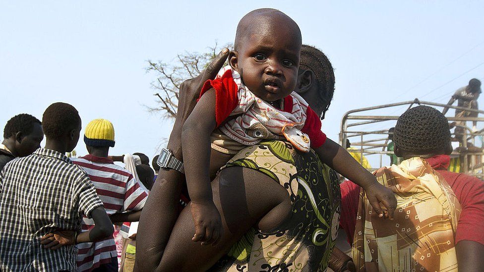 A woman holds a baby as refugees from South Sudan wait to board a truck at Dzaipi Refugee Transit Centre in Adjumani, northern Uganda, to be transferred to nearby Nyumanzi Resettlement Camp
