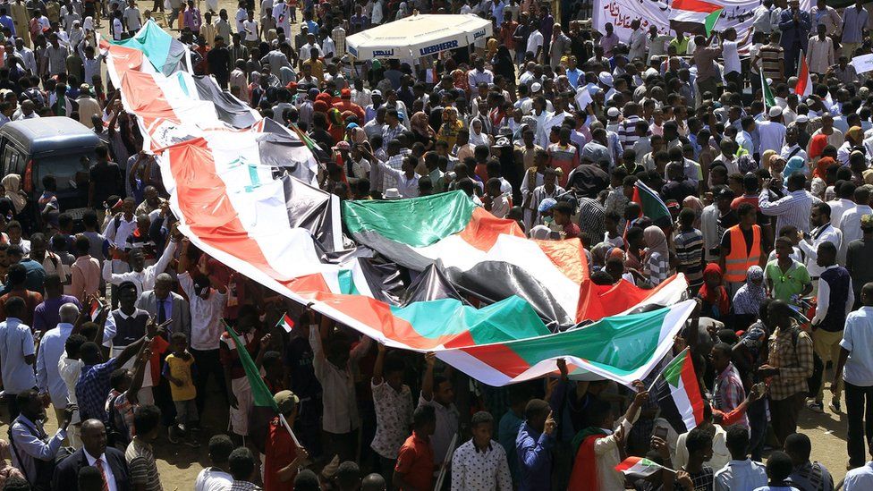 Sudanese protesters deploy their national flag as they protest outside the army headquarters in Khartoum