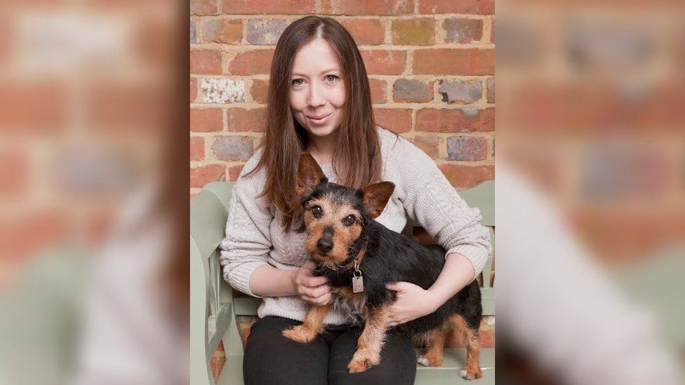 Amy Hyde sat on a green bench with a terrier on her lap.