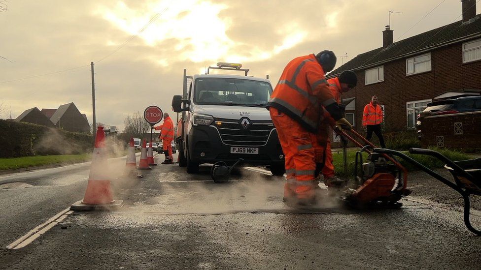 A road maintenance crew in Swindon with their truck fixing a pothole and helping traffic round.