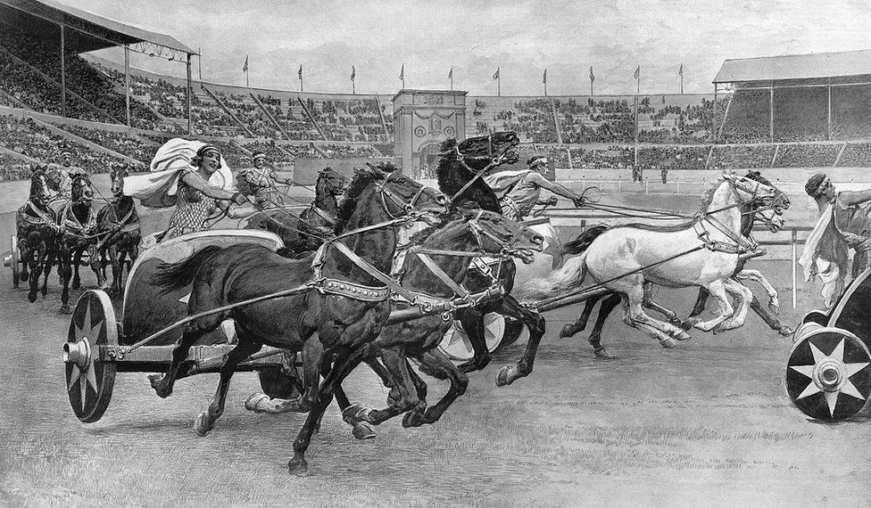 Black and white illustration of men and women dressed as Romans during a chariot race around Wembley Stadium