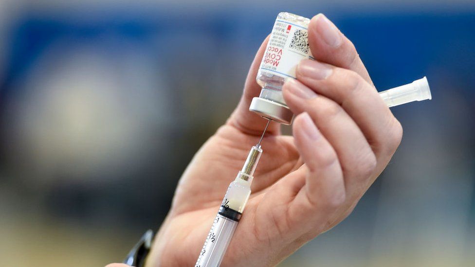 A hand shown filling a syringe with Moderna Covid-19 vaccine from a glass vial