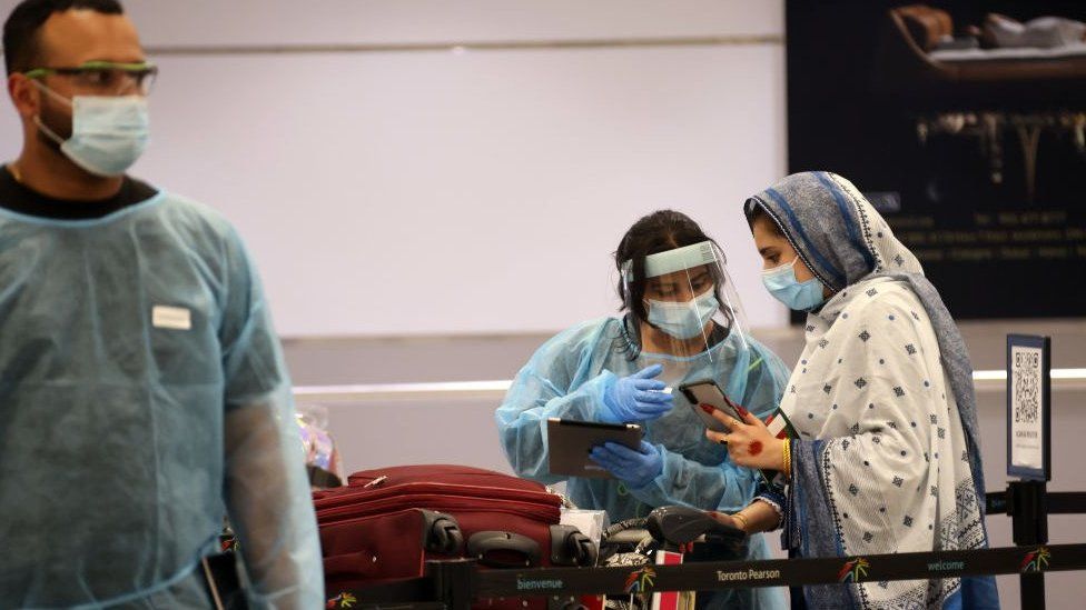 Медицинский работник в маске направляет путешественника в маске, прибывающего в международный аэропорт Торонто Пирсон в Канаде.