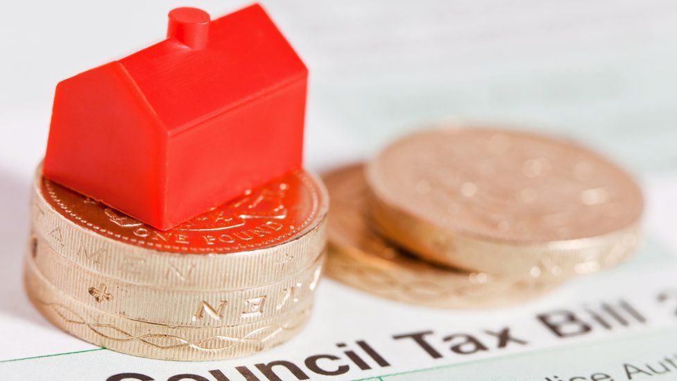Pound coins are piled up on top of a council tax bill and topped with a small red plastic house.