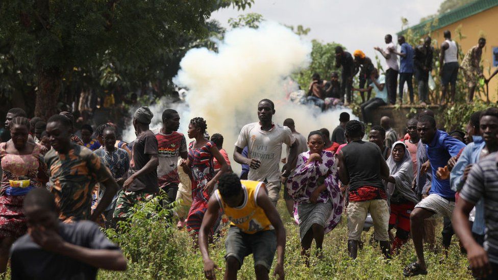 People run from a tear gas shot by Nigerian police officers during a mass looting of a warehouse that have COVID-19 food palliatives that were not given during lockdown to relieve people of hunger, in Abuja, Nigeria, on October 26, 2020.