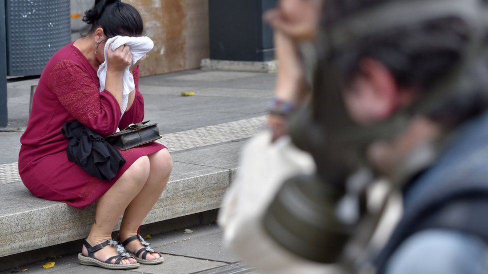 Una mujer que sufre los efectos del gas lacrimógeno se tapa la cara con un trapo blanco, mientras está sentada en una vereda.