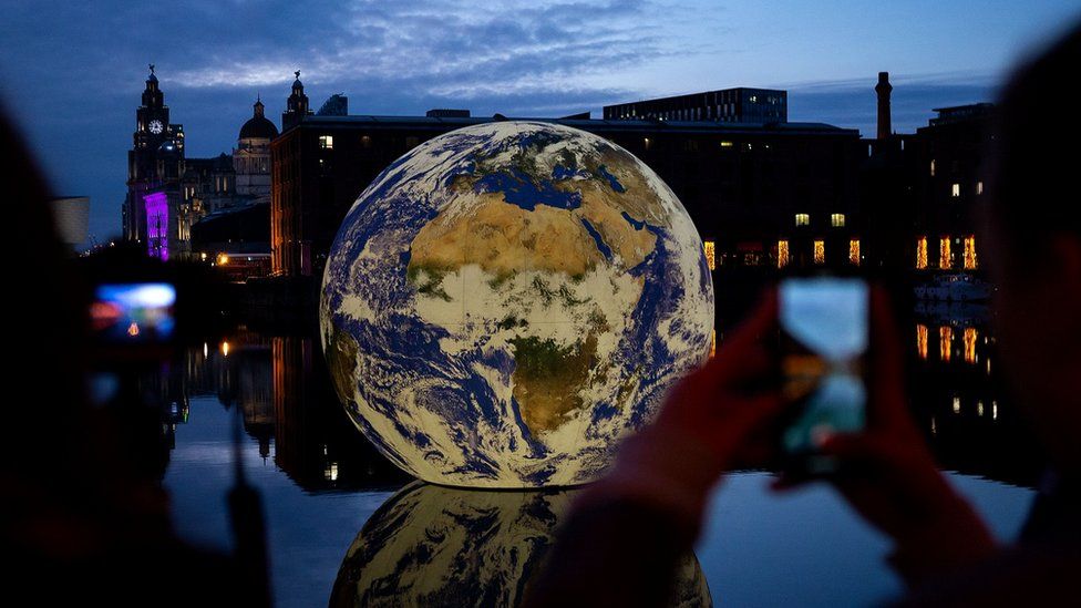 People take photographs of the installation 'Floating Earth' by artist Luke Jerram at the Royal Albert Dock in Liverpool, Britain, 28 April 2023