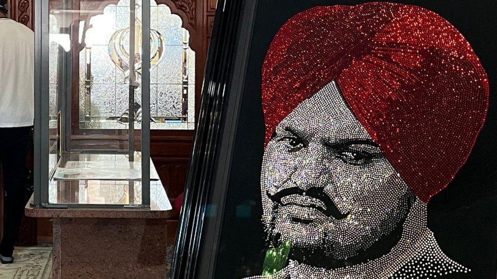 A mosaic portrait on a black background made up of hundreds, possibly thousands of small gemstones. It is a likeness of Sidhu Moose Wala - his turban is a deep ruby red and the rest of his face has been recreated using silver-white gems, giving it the appearance of a black-and-white photograph.
