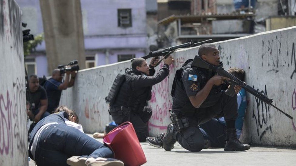 Policemen and journalists take cover during an operation to fight heavily armed drug traffickers at the Rocinha favela in Rio de Janeiro, Brazil, on September 22, 2017.