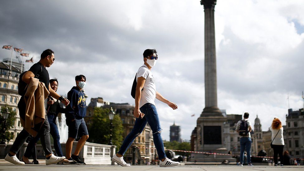 People wearing protective face masks walks through Trafalgar Square