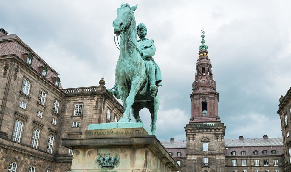 Вид вверх на дворец Кристианборг с памятником королю Кристиану Ix на переднем плане.