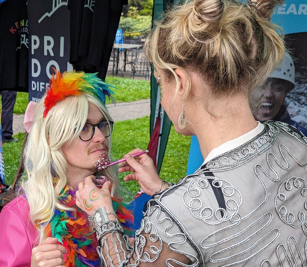Someone getting their face painted with in rainbow colours