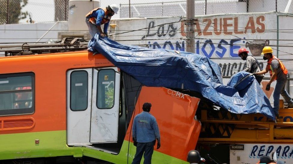 Workers cover a damaged train car after been moved from a site where an overpass for a metro partially collapsed with train cars on it at Olivos station in Mexico City