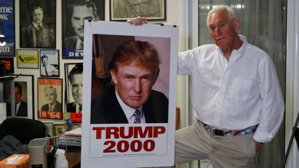 Roger Stone holding a Trump 2000 campaign poster