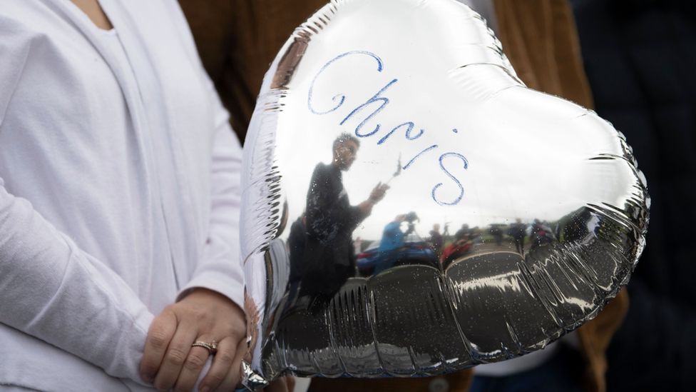 A person holds a balloon which says "Chris"