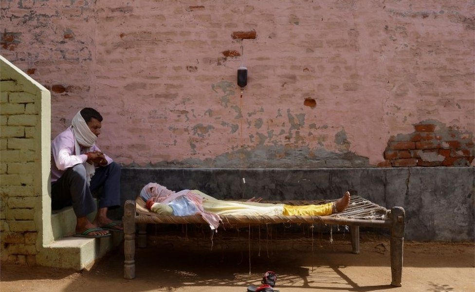 Мужчина сидит рядом со своей женой, которая страдает от лихорадки, когда она проходит лечение в клинике, созданной местным сельским жителем на фоне распространения коронавирусной болезни (COVID-19), в деревне Парсаул в Большой Нойде, на севере страны. штат Уттар-Прадеш, Индия, 22 мая 202 г.