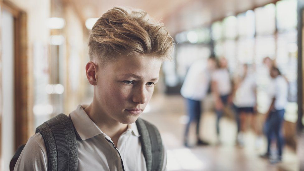 At school, a teenage boy looks sad, with other students in the background